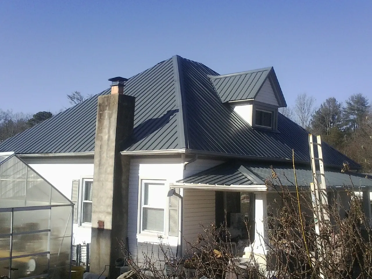 Dark blue standing seam metal roof on a white farmhouse with dormer — Slate & Tile Roof Repair by Roofing Brothers in Olney Springs
