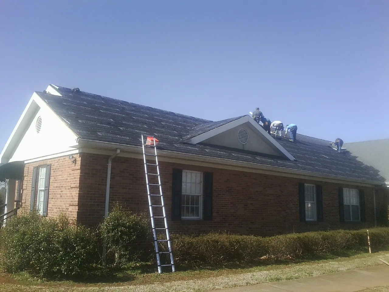 Crew tearing shingles off a brick ranch roof with a ladder set — Emergency Roof Repair work by our crew in Olney Springs