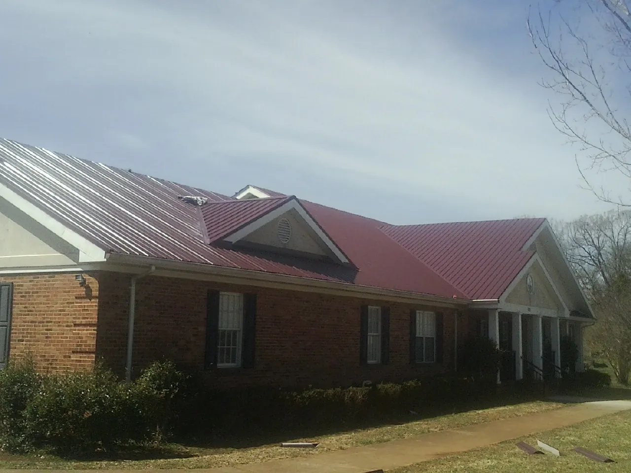Red metal roof with gabled entries on a long brick building, from a Hail Damage Roof Repair job in Olney Springs