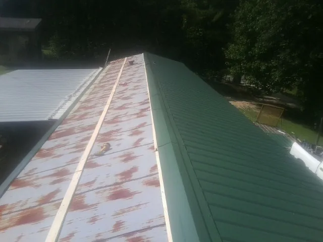 Old rusted panels beside newly installed green metal roofing — Wind Damage Roof Repair by Roofing Brothers in Olney Springs