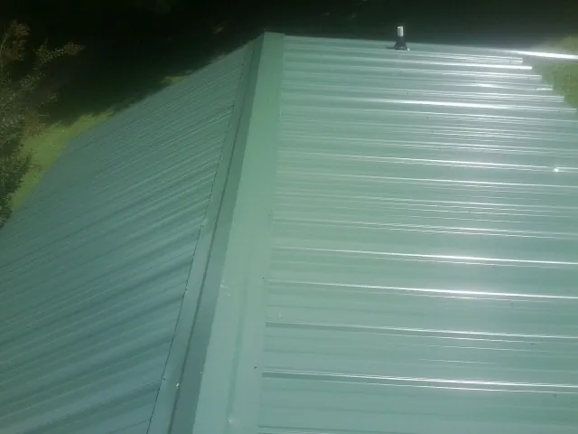 New green metal panels meeting at the ridge of a roof — Flat Roof Repair work by our crew in Olney Springs