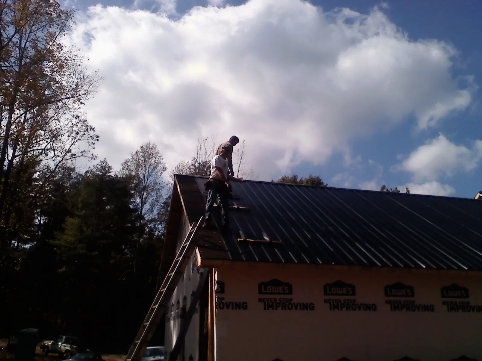 Roofer fastening dark metal panels high against a cloudy sky, from a Roof Inspection job in Olney Springs