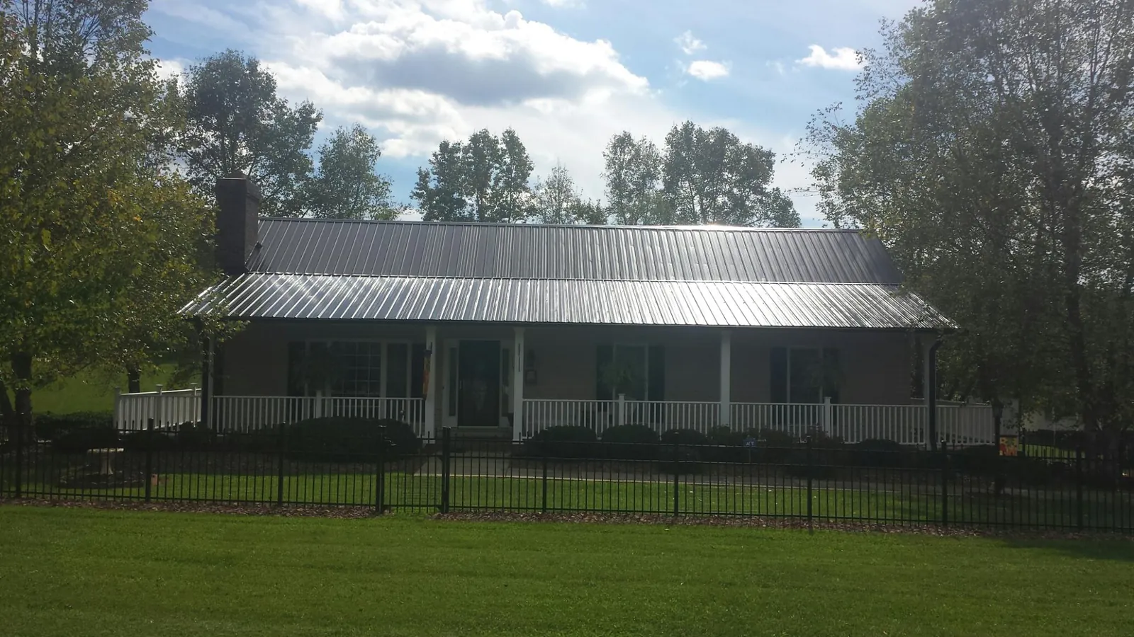 Gray metal roof on a brick ranch with a full width front porch — Gutter Guard Installation work by our crew in Olney Springs
