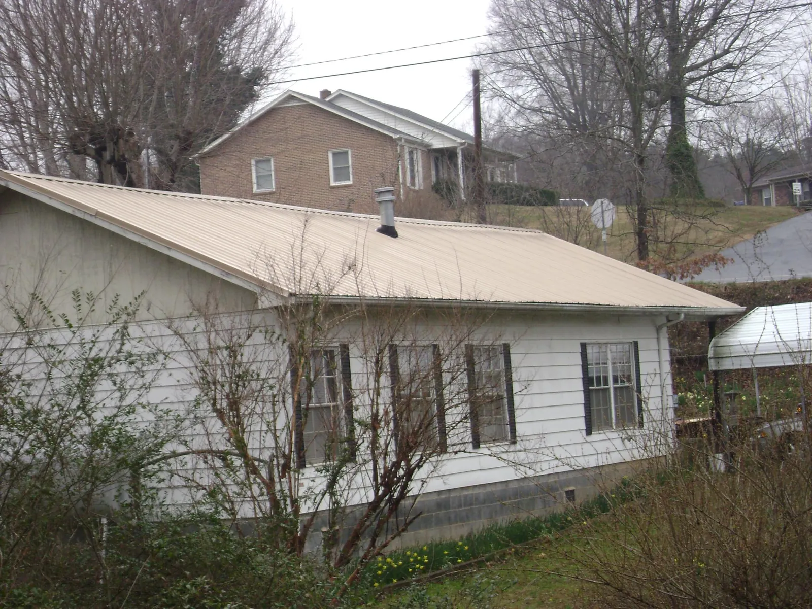 Tan metal roof on a white sided house set into a hillside — Commercial Roofing by Roofing Brothers in Olney Springs