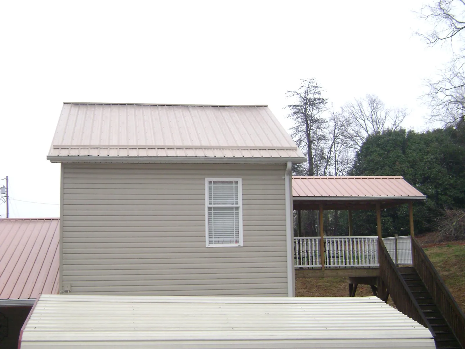 Tan metal roofs on a two story addition and attached porch, from a Roof Replacement job in Olney Springs